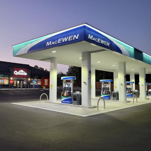 MacEwen gas station at dusk featuring a blue and white fuel canopy, multiple gas pumps, and a Quickie convenience store in the background.