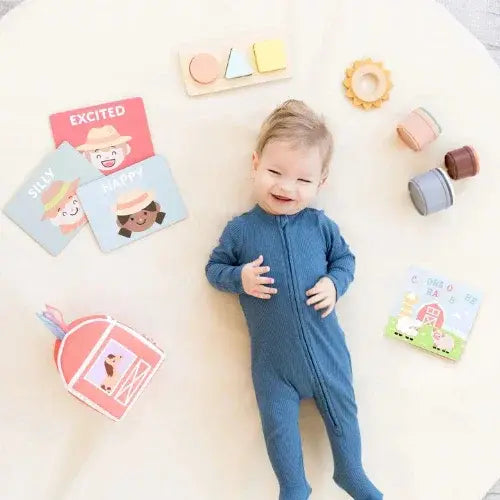 Baby in a blue onesie surrounded by educational toys and books on a white surface