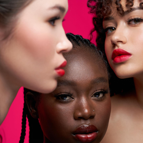 Three women with vibrant makeup against a pink background