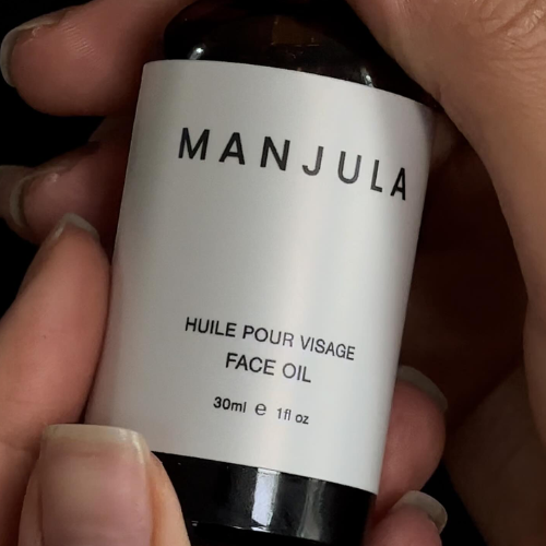 Manjula face oil bottle held by hands with a dark background