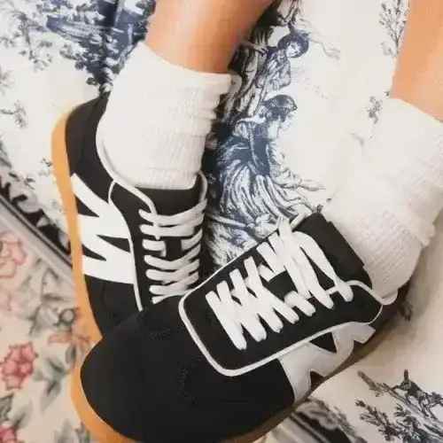 Black and white sneakers with brown soles worn by a person with white socks on a patterned surface.