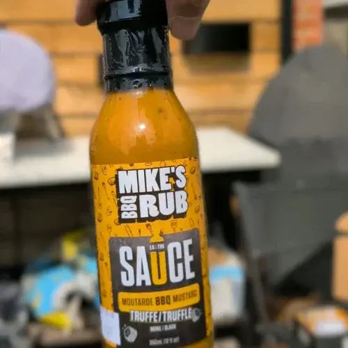 A hand holding up a Bottle of Mike's BBQ Rub against a wooden background