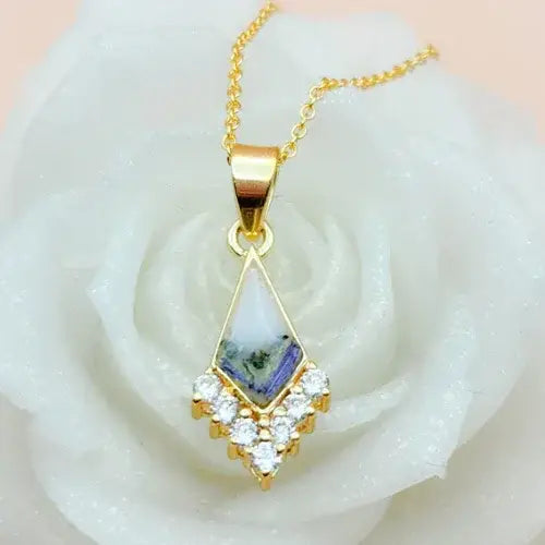 Gold pendant with a central gemstone and diamond-like stones on a white rose.