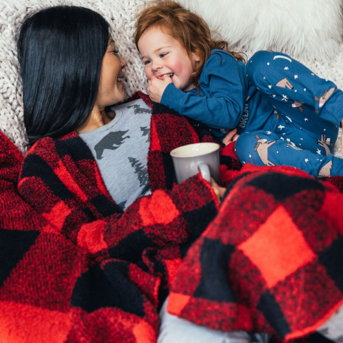 Woman and child lying on a blanket, both wearing red and black checkered pajamas.