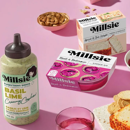 Millsie brand products including a bottle of basil lime sauce, boxes of dips, and a bowl of nuts on a pink background.