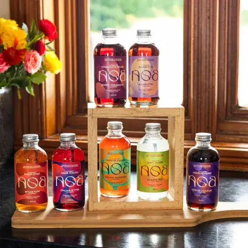Assorted bottles of NSA drinks on a wooden stand with flowers in the background.