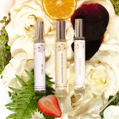 Three perfume bottles on a bed of white flowers with a strawberry and orange slice.