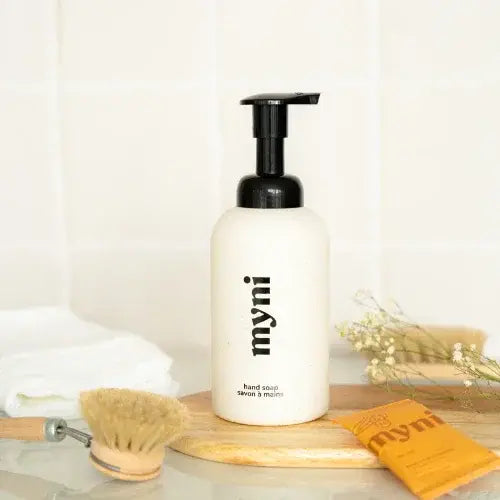 Bottle of myni hand soap stting on wooden board in front of bright white wall