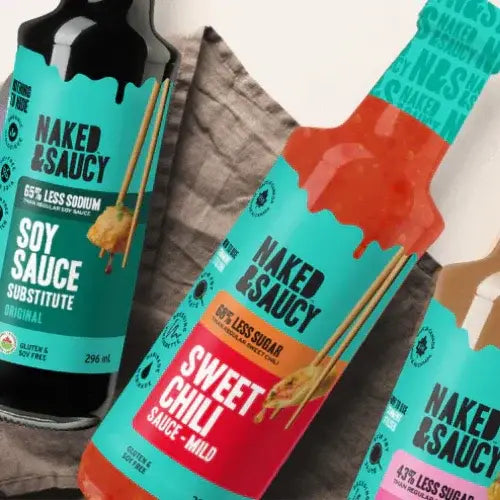 Naked & Saucy sauce packages including Soy Sauce Substitute and Sweet Chili Sauce on a wooden surface.