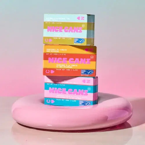 Stack of colorful 'Nice Cans' boxes on a pink platform with a gradient background