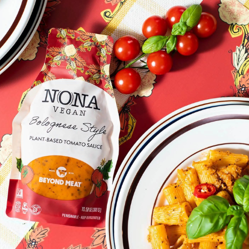 Nona Vegan Bolognese Style plant-based tomato sauce package with pasta and tomatoes on a decorative table.