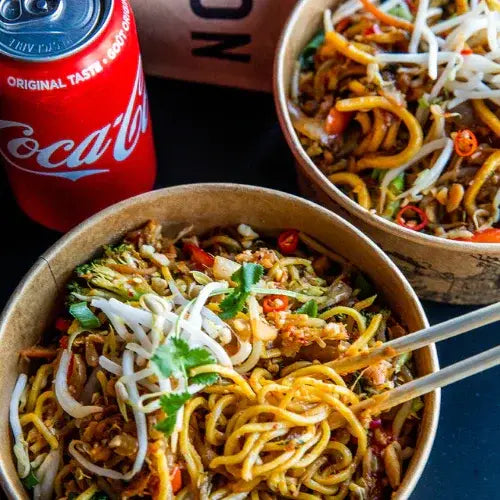 Two bowls of noodles with a can of Coca-Cola on a dark surface