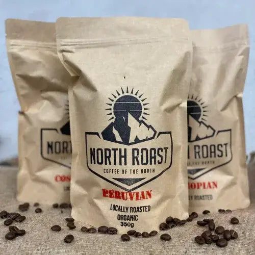 Three 'North Roast' coffee bags with coffee beans on a textured surface