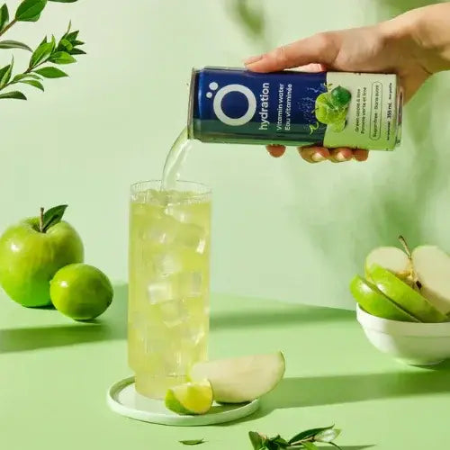 Person pouring a drink from a box labeled 'O Hydration' into a glass with green apples and leaves on a light green background.