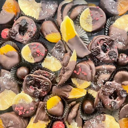 Assorted oenomel chocolate candies with orange slices and sprinkles on a dark surface