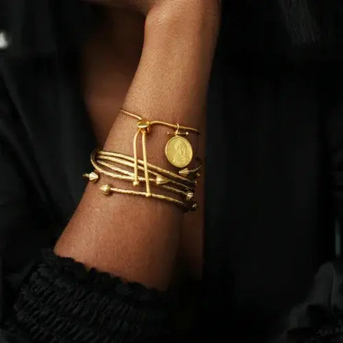 Stacked gold bracelets with African coin pendant on model’s wrist – Ethically handmade heirloom jewellery by Canadian-owned Omi Woods