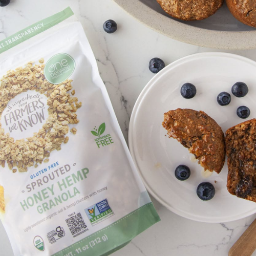 Bag of sprouted honey hemp granola next to a plate with granola and blueberries on a marble surface