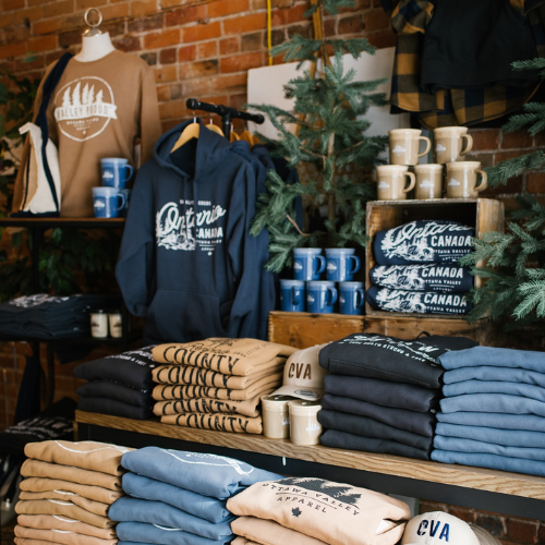 Display of folded clothing and mugs with branding in a store setting.