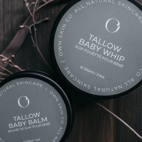 Two containers of Tallow Baby Whip and Tallow Baby Balm from Own Skin Co. on a dark background.