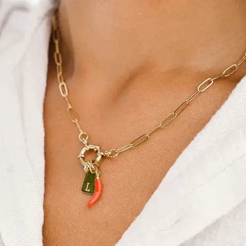 Gold chain necklace with a red chili pepper charm on a person wearing a white top.