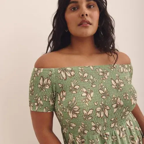 Woman wearing a green floral off-shoulder dress against a plain background