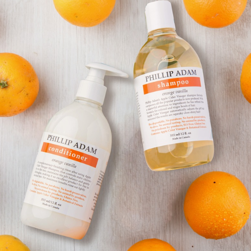Two bottles of Phillip Adam shampoo and conditioner with oranges on a light wooden surface.