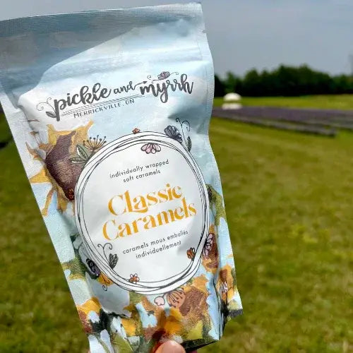 Pack of pickle and myrrh classic caramels held in front of a grassy field.