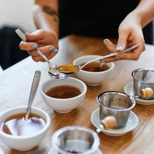 Person preparing a cup of tea with various utensils on a wooden table.