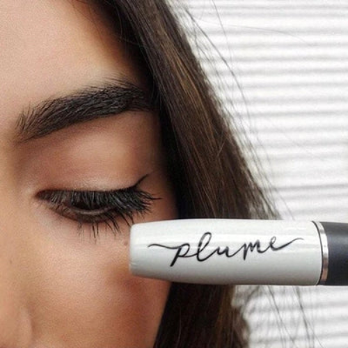 Eyelash serum pen with 'plume' branding held near an eye