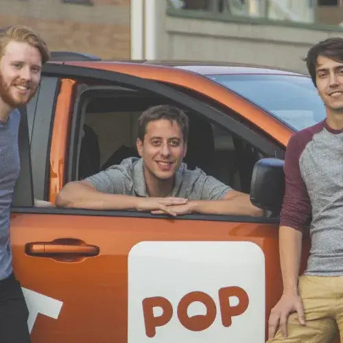 Three men standing next to an orange car with a 'POP' logo.
