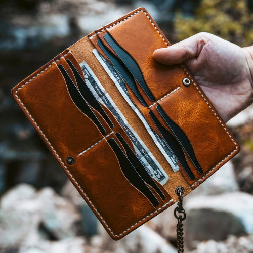 Brown leather wallet with coins and cards held by a hand against a blurred natural background