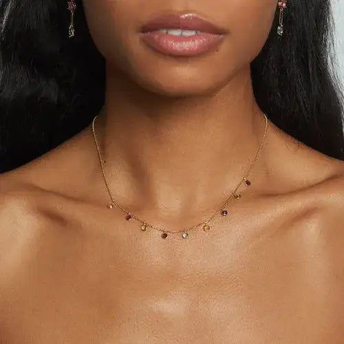 Close-up of a woman wearing a delicate gold necklace with small colored beads.