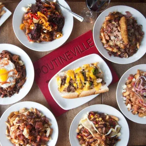 A table filled with a variety of gourmet poutines and a cheesy sandwich at Poutineville, each dish topped with unique ingredients like eggs, pulled meat, grilled vegetables, cheese, and gravy, arranged around a red placemat with 'POUTINEVILLE' written on it.