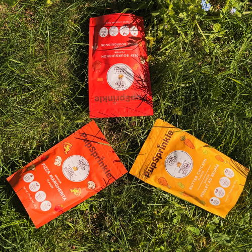 Three red and orange packages labelled 'PupSprinkle' on grass