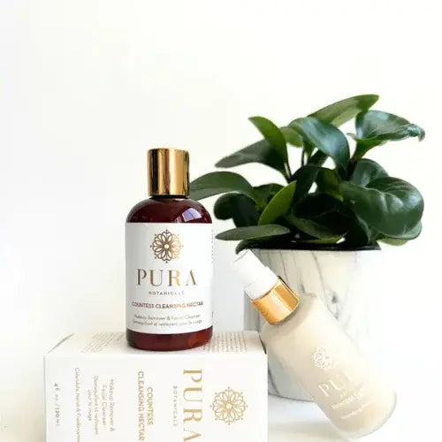 Pura Botanicals natural skincare products with cleansing nectar bottles displayed beside a green potted plant