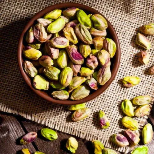 Pistachios in a brown bowl on a textured fabric background