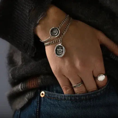 Hand wearing multiple silver bracelets and a ring on a dark background