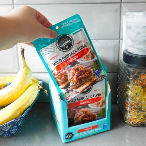 Hand reaching for a packet of wild skipjack tuna with a light background