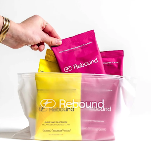 Hand picking a pink 'Rebound' protein mix packet from a clear bag on a white background