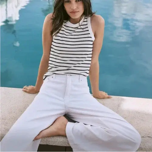 Woman in Reitmans striped tank top and white wide-leg jeans relaxing by a poolside in summer fashion