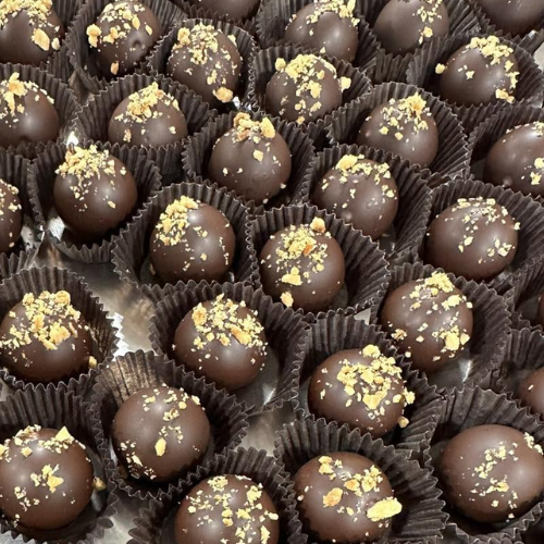 A close-up arrangement of chocolate truffles in dark brown paper cups, each topped with coarse golden crumbs.