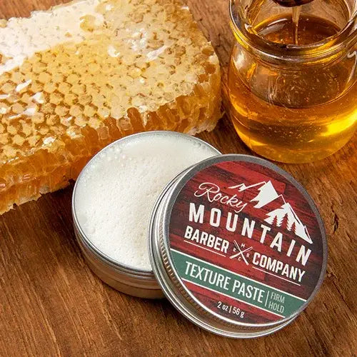Texture paste tin from Rocky Mountain Barber Company with honeycomb and jar of honey on a wooden surface