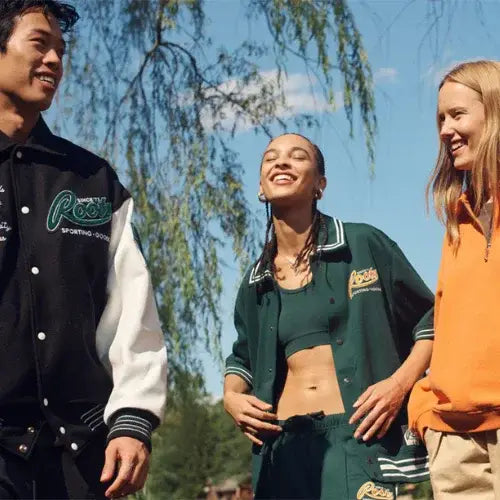 Group of friends wearing sporty Roots apparel outdoors, featuring varsity jackets, track pants, and casual athleticwear