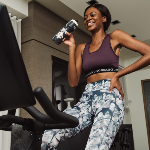 Woman in Samsara branded athletic wear holding a water bottle on a stationary bike.