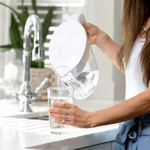 Person pouring water from a clear pitcher into a glass in a kitchen.