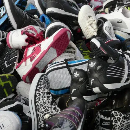 A large pile of assorted athletic and casual sneakers in various colours and styles, including brands like Adidas, Nike, and Puma. Some shoes feature bold patterns like leopard print or bright accents such as pink soles and purple laces.