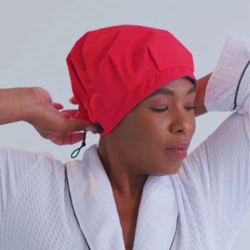 Person wearing a red skippper shower cap, adjusting it.