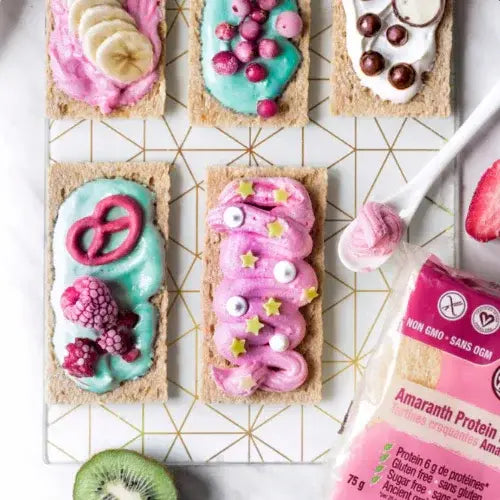 Smartbite crispbreads with colourful frosting and toppings on a geometric patterned surface, with a package of Amaranth crispbreads in the foreground.