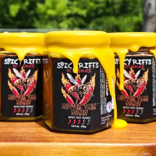 Three jars of Spicy Riffs Hot Sauce on a wooden surface with a blurred green background