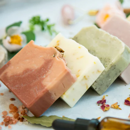 Assorted bars of soap on a white surface with dried flowers and leaves.